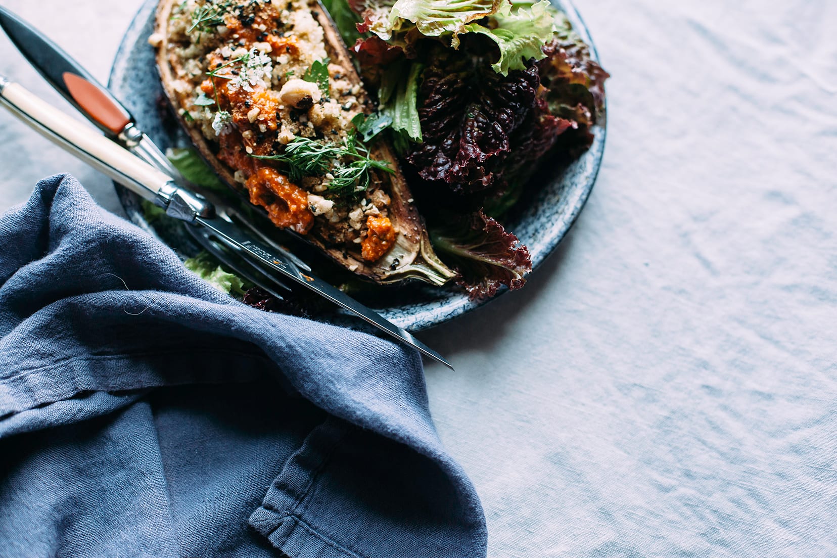 Image shows a stuffed eggplant "boat" with a salad served alongside, on a blue plate.