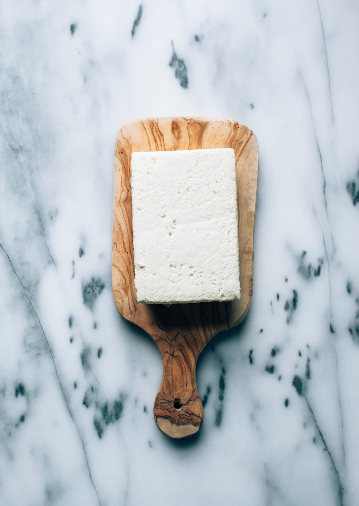 An overhead shot of a block of tofu on a small wooden cutting board.