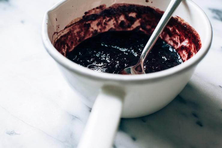 A 3/4 angle shot of a jammy blueberry bbq sauce in a white enamelware pot.
