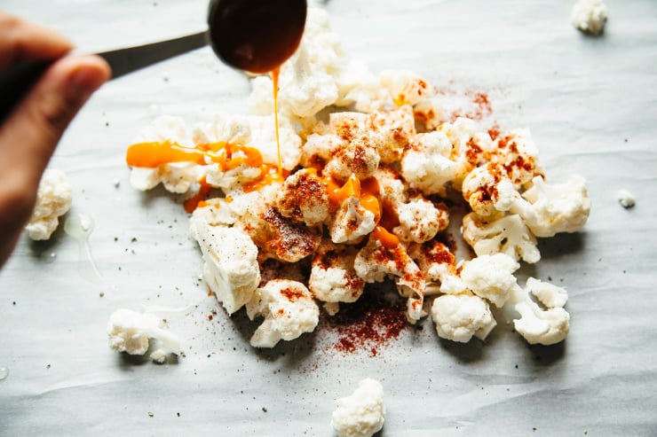 Image shows a hand spooning some hot sauce on top of some cut cauliflower florets.