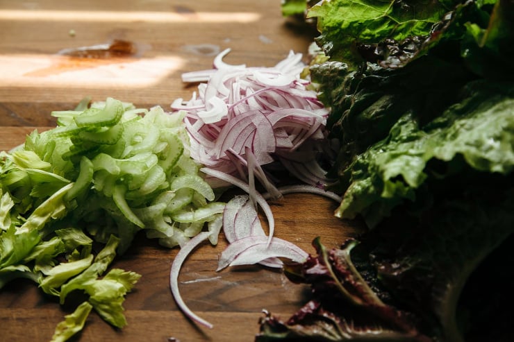 Image shows cut celery, red onions and lettuce on a wooden cutting board.
