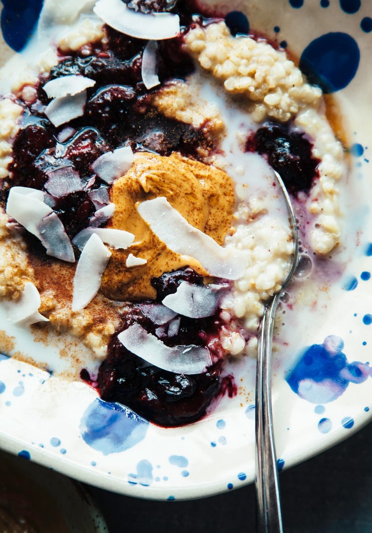 An up close, overhead shot of a bowl of creamy porridge topped with fruit compote, peanut butter and large coconut flakes. Part of a lentil recipes roundup.