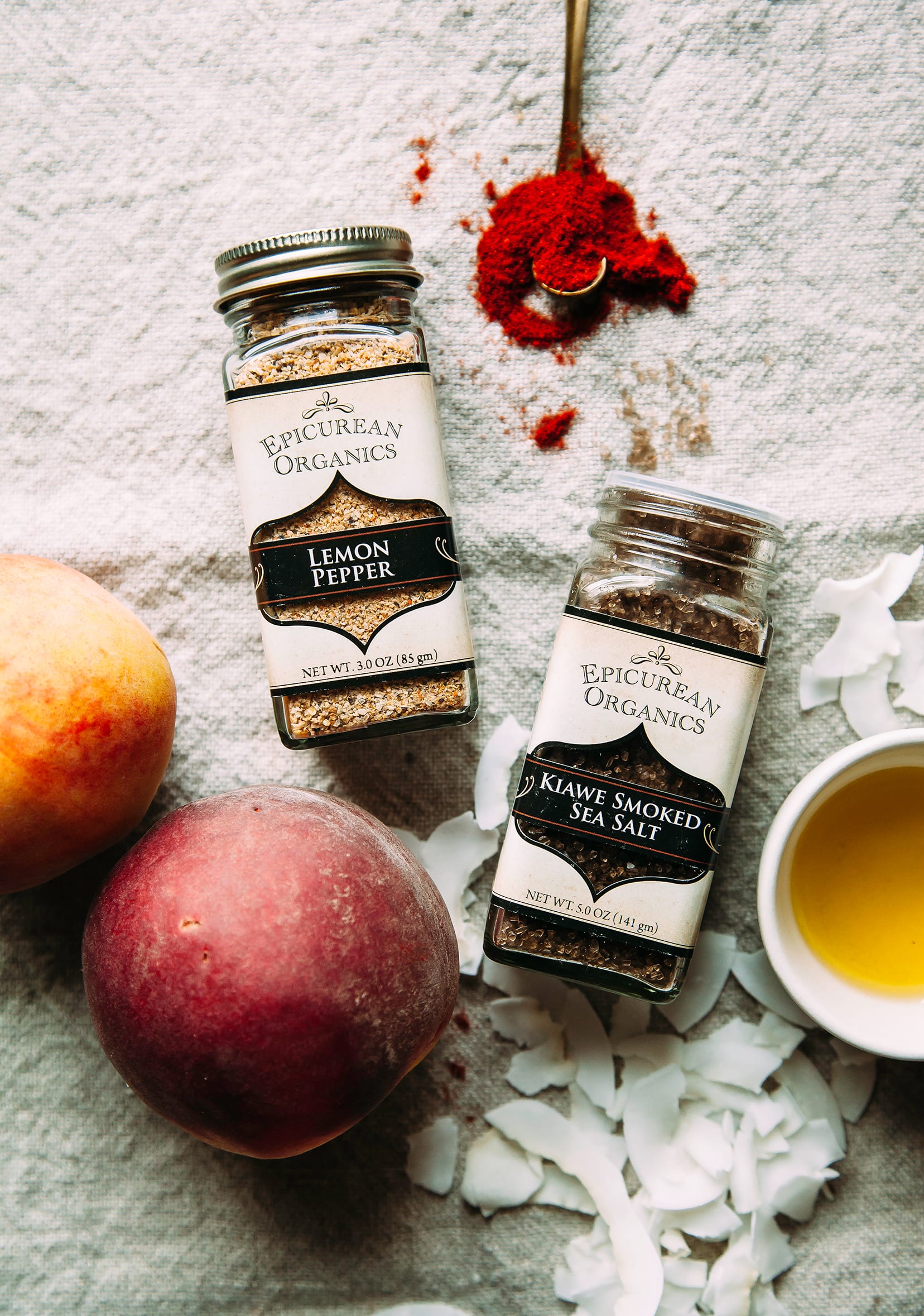 An overhead shot of spice jars from Mountain Rose Herbs, next to some peaches and a small bowl of oil.