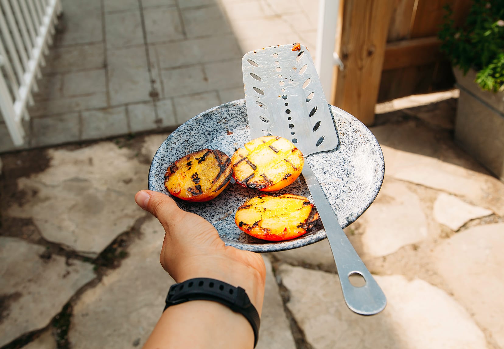 Image shows a hand holding a plate with grilled peach halves on it.
