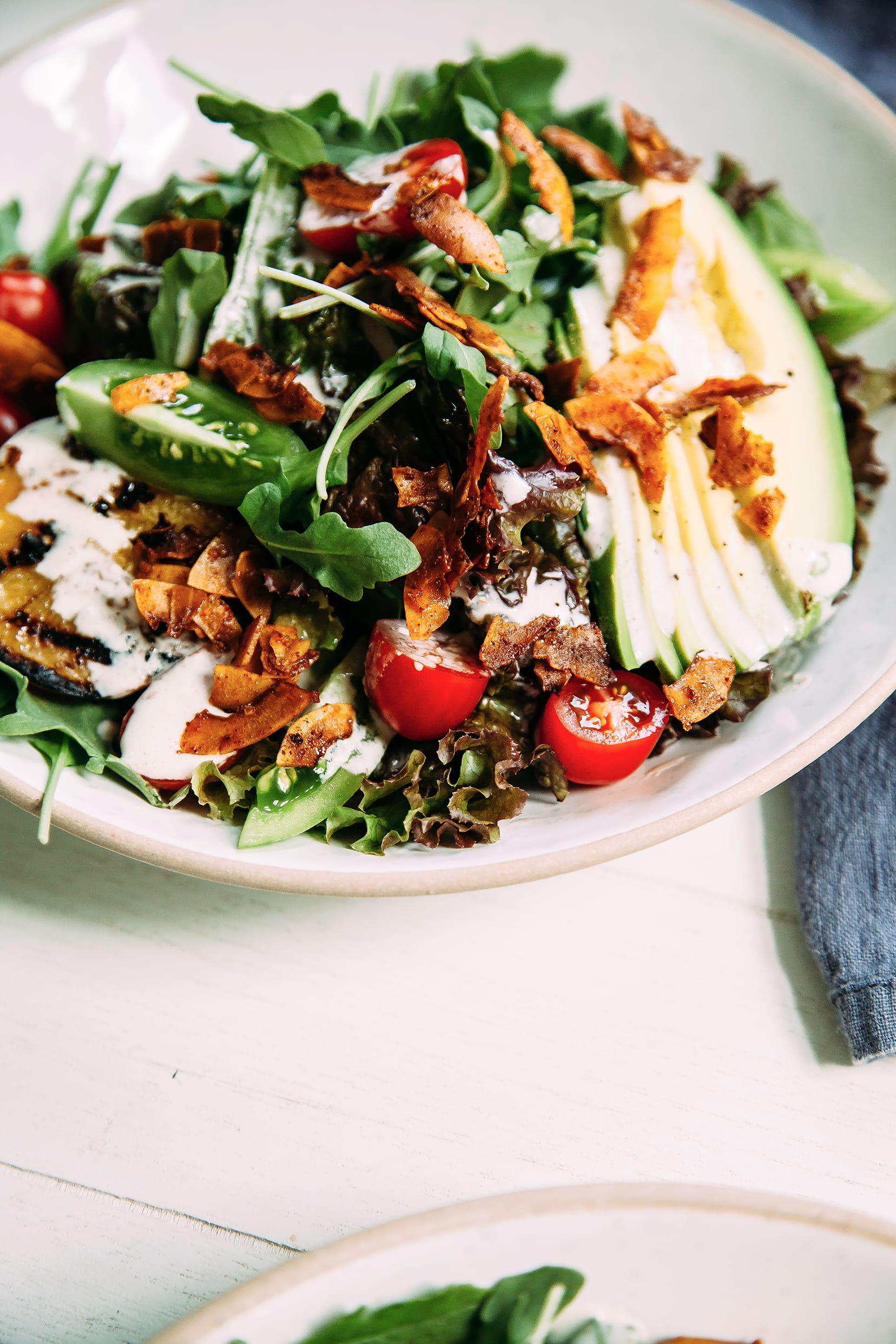 A 3/4 angle, up close shot of a vegan BLT salad topped with browned coconut "bacon" bits and a creamy white dressing.
