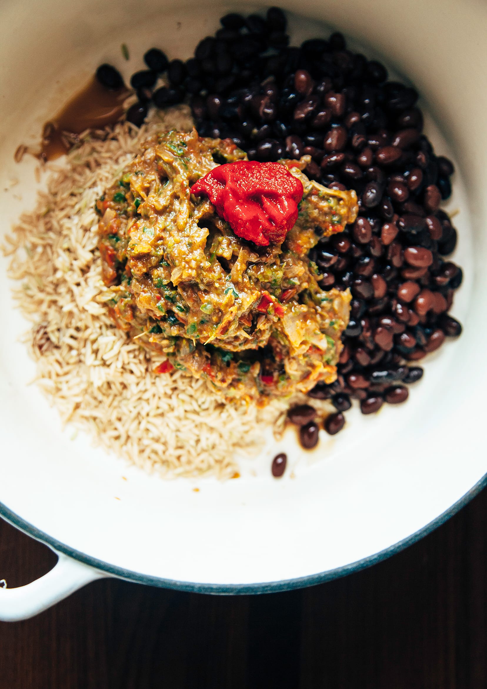 An overhead image of brown rice, black beans, and a pureed roasted vegetable flavour base inside a white Dutch oven-style pot.