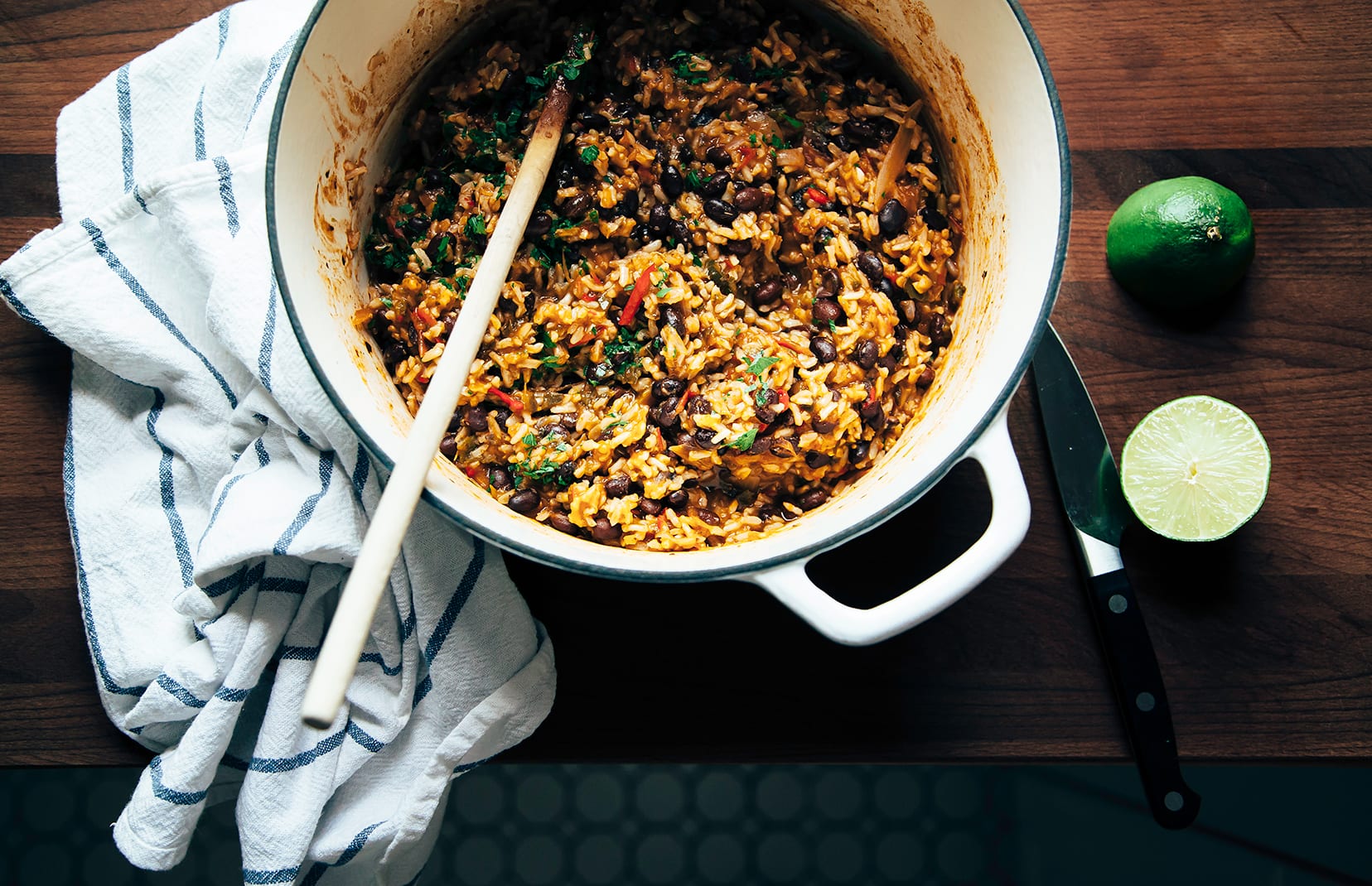 An overhead shot of black beans and rice with some herbs and vegetables in a Dutch oven-style pot on a dark wood background.