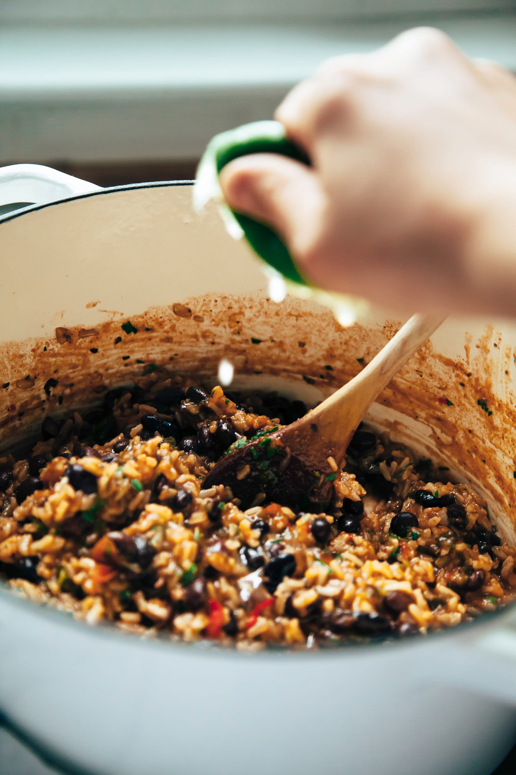 Image shows a hand squeezing a lime half into a pot of black beans and rice.