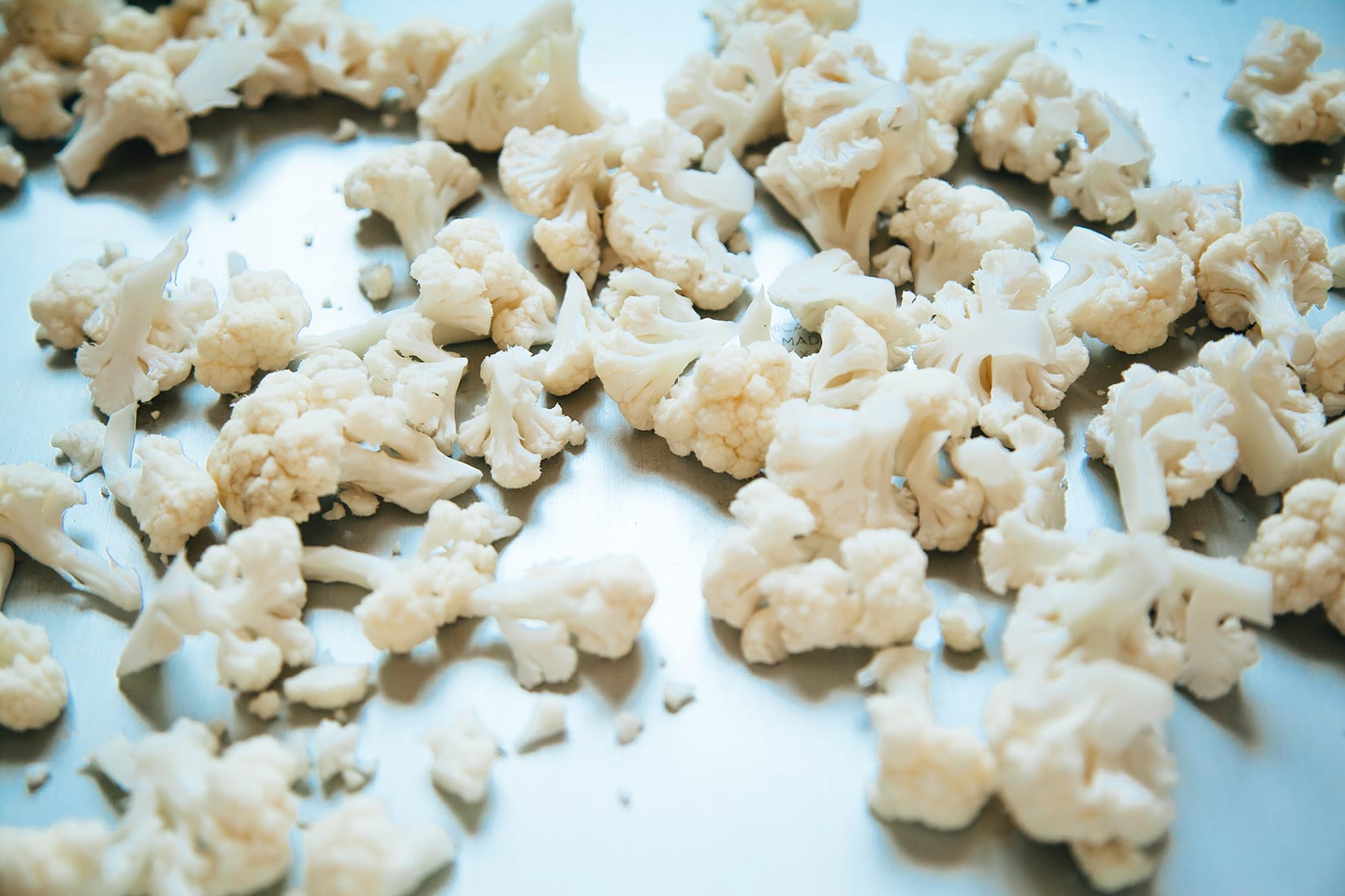 Image shows cauliflower florets on a baking sheet.