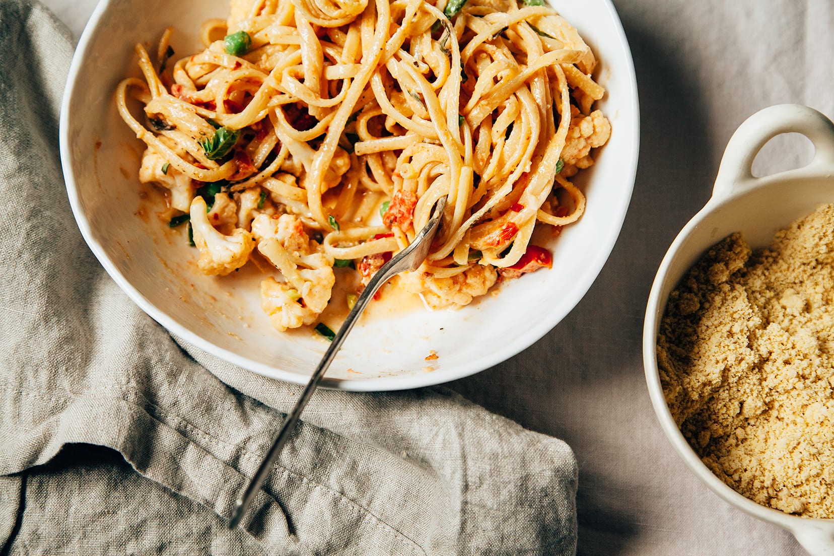 Image shows an individual serving of creamy cauliflower pasta with basil, peas, and tomatoes.