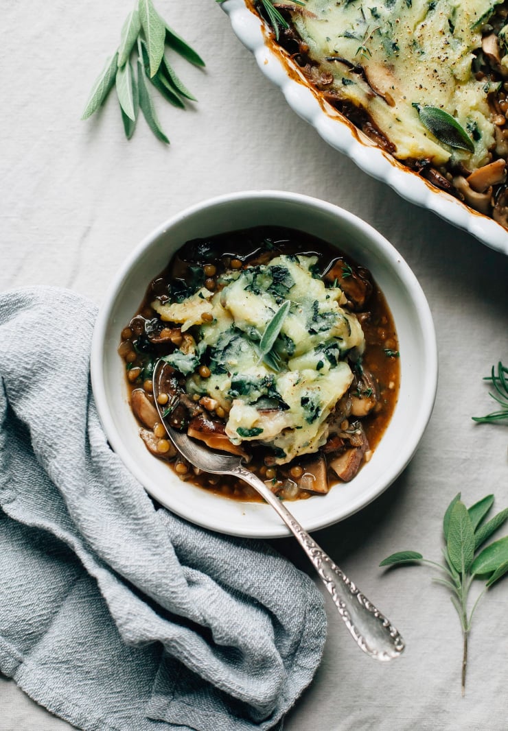 An individual serving of mushroom gravy pie topped with a dollop of mashed potatoes with kale. There is a grey linen napkin nearby.