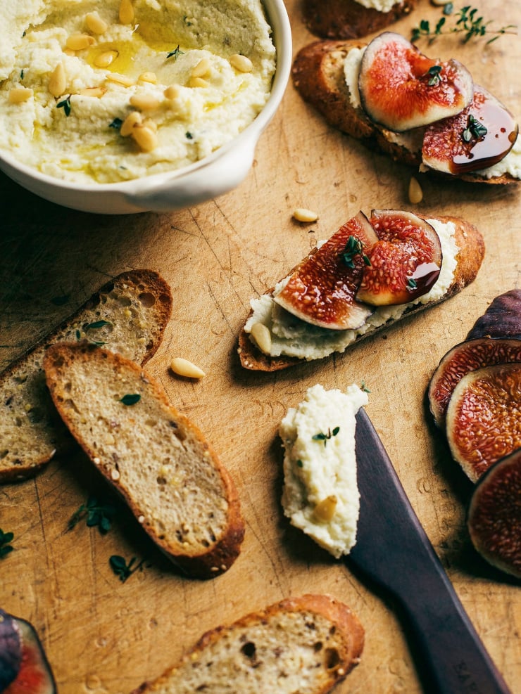 An overhead shot of creamy vegan ricotta swooped on crostini’s with slices of fig on top.