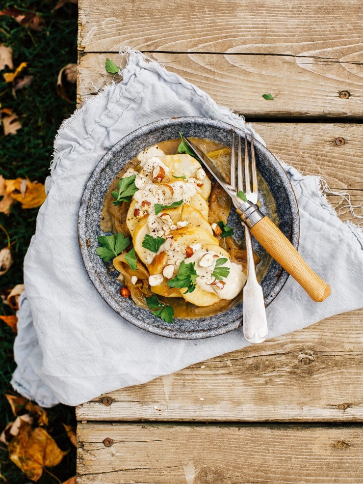 Image shows sliced roasted celery root on a plate with a creamy sauce on top.