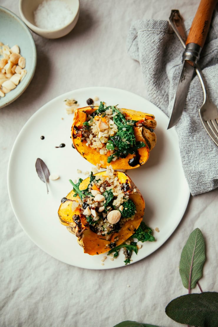 An overhead shot of two stuffed roasted squash halves filled with quinoa and almonds. Part of a roundup of vegan holiday recipes