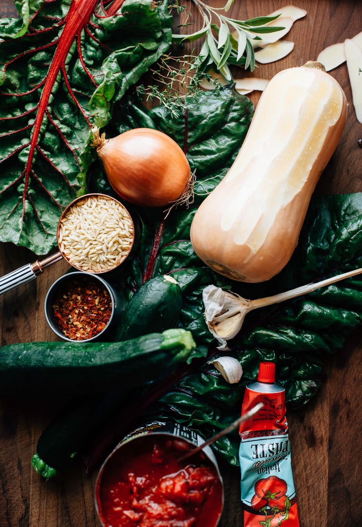 An overhead shot of ingredients for butternut minestrone on a dark wood cutting board.