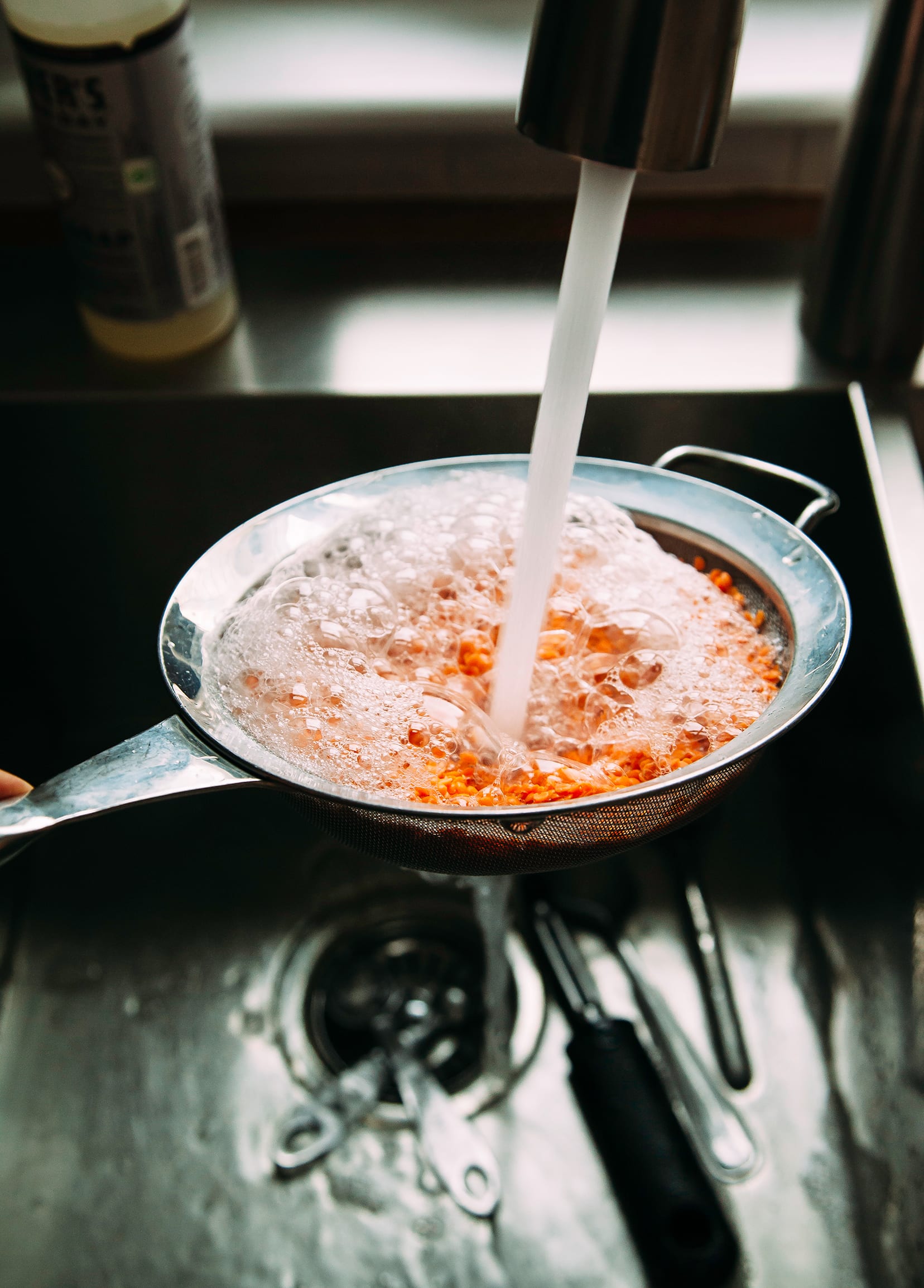 Image shows red lentils being rinsed under a faucet.