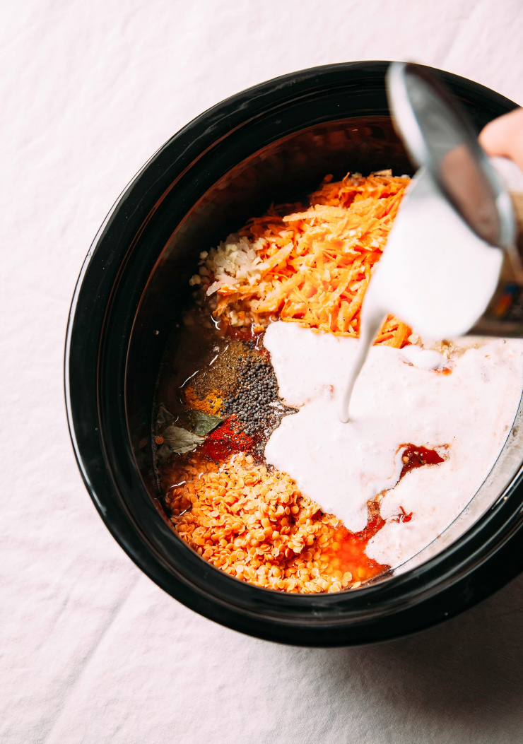 Image shows a can of coconut. Milk being poured into a slow cooker insert, along with other soup ingredients.