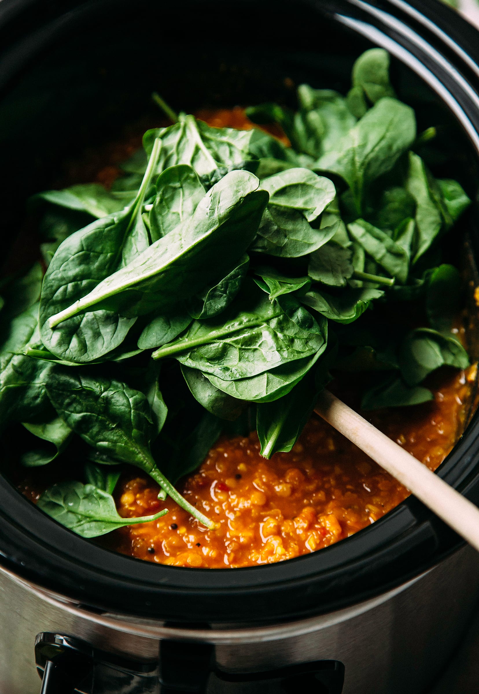 Image shows baby spinach being added to a lentil soup.