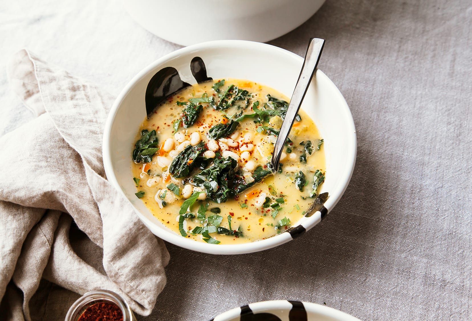 A 3/4 angle shot of an individual serving of creamy white bean soup. A beige napkin is nearby.