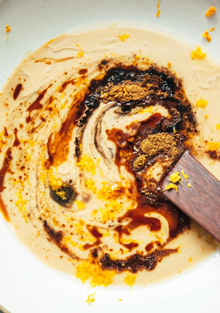 An overhead shot of spices and maple syrup being stirred into tahini, creating a swirl effect.