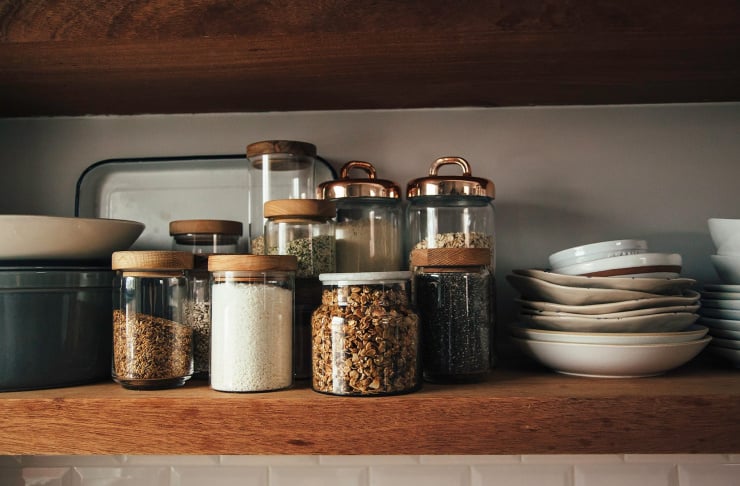 Image shows an open kitchen shelf with jars of seeds, grains, coconut, and granola.
