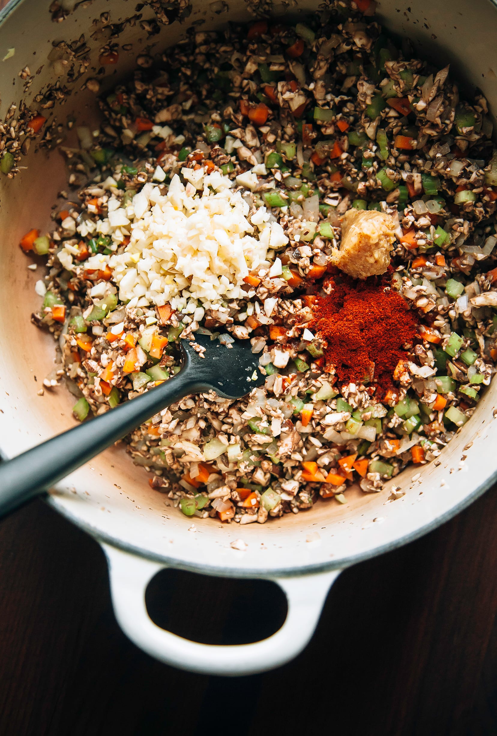 An overhead shot of mushrooms, celery, onions, carrots, and garlic sautéing in a beige Dutch oven.
