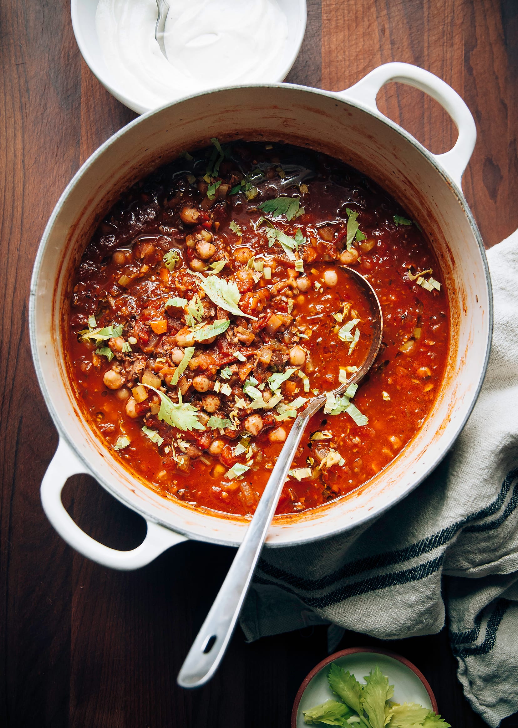 AN overhead shot of Buffalo chickpea chili with mushrooms in a beige Dutch oven on a dark wood background.