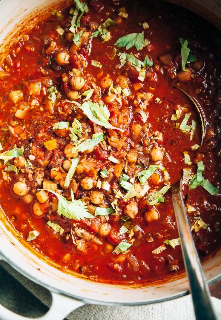 An up close, overhead shot of Buffalo chickpea chili in a beige Dutch oven. There is a ladle sticking out of the pot.