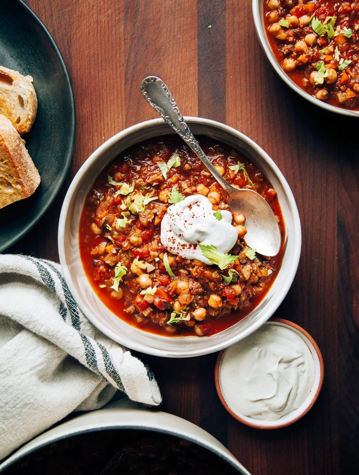 An overhead shot of Buffalo chickpea chili in a wide bowl with a piece of toasted bread on top. There’s also a bright white dollop of cashew four cream.