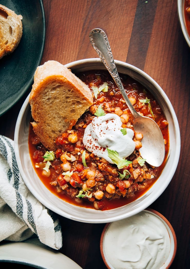 An overhead shot of Buffalo chickpea chili in a wide bowl with a piece of toasted bread on top. There’s also a bright white dollop of cashew four cream.
