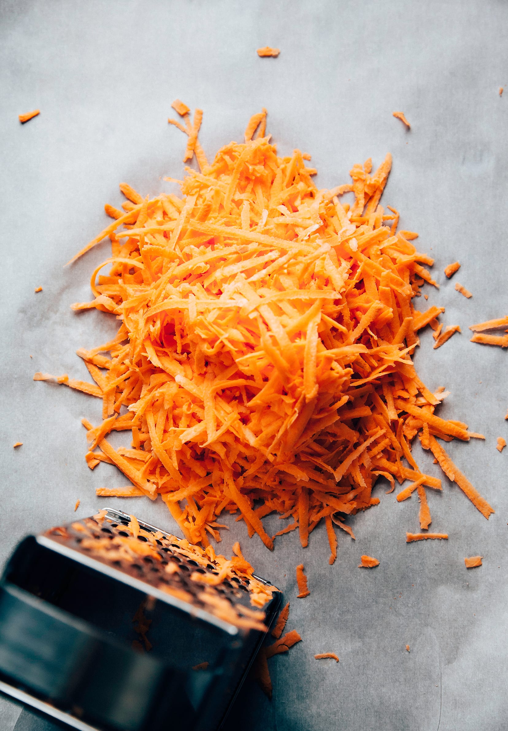 An overhead shot of shredded sweet potatoes and a box grater to the side.