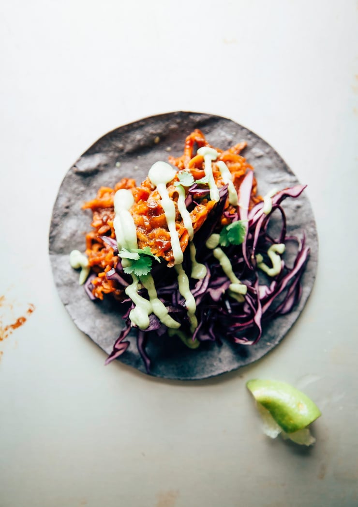 An overhead shot of a single taco with a saucy sweet potato filling, shredded purple cabbage and a drizzle of a light green, creamy sauce over the top.