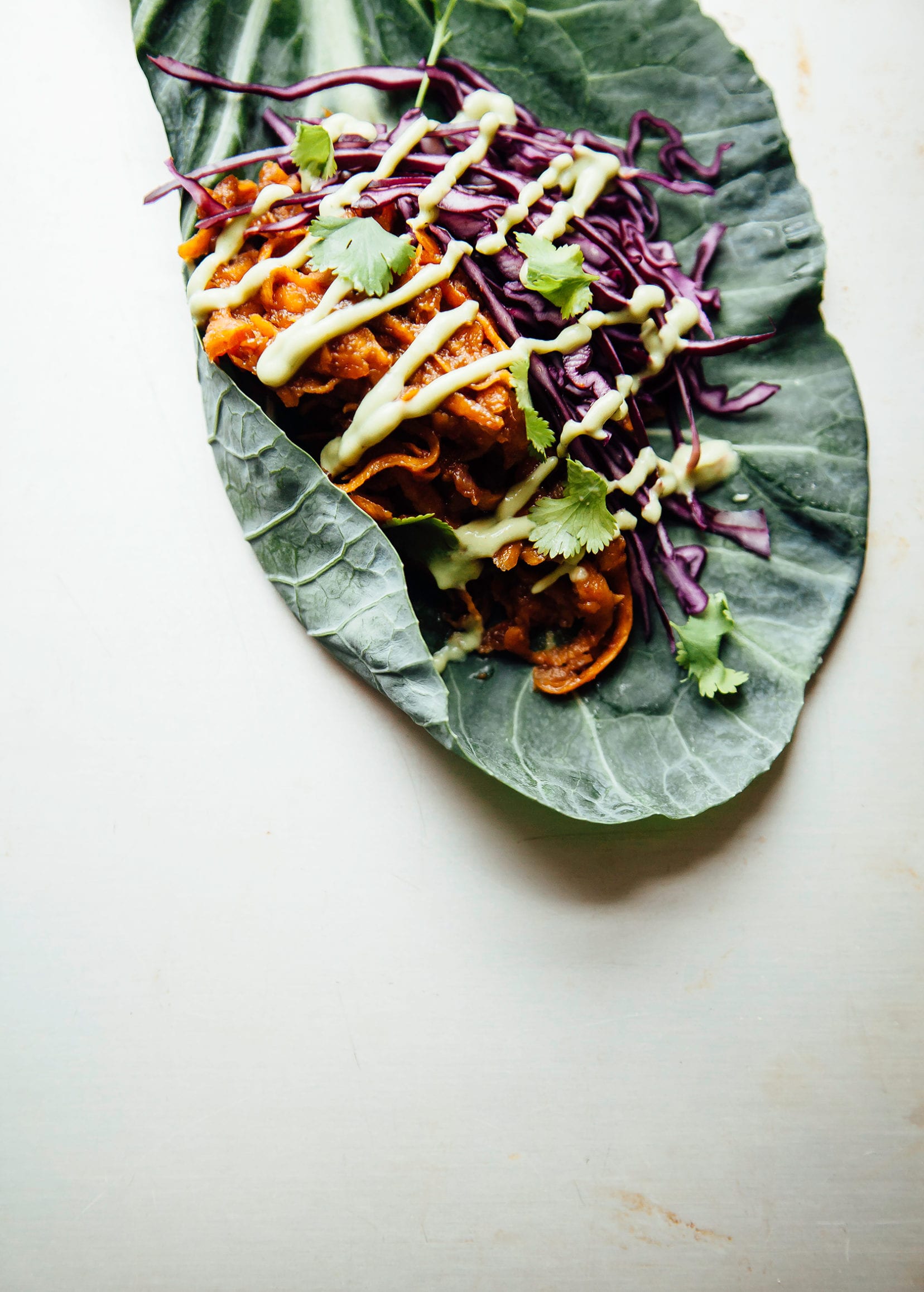 An overhead shot of a sauce sweet potato filling, shredded cabbage, and creamy sauce inside of a collard leaf.