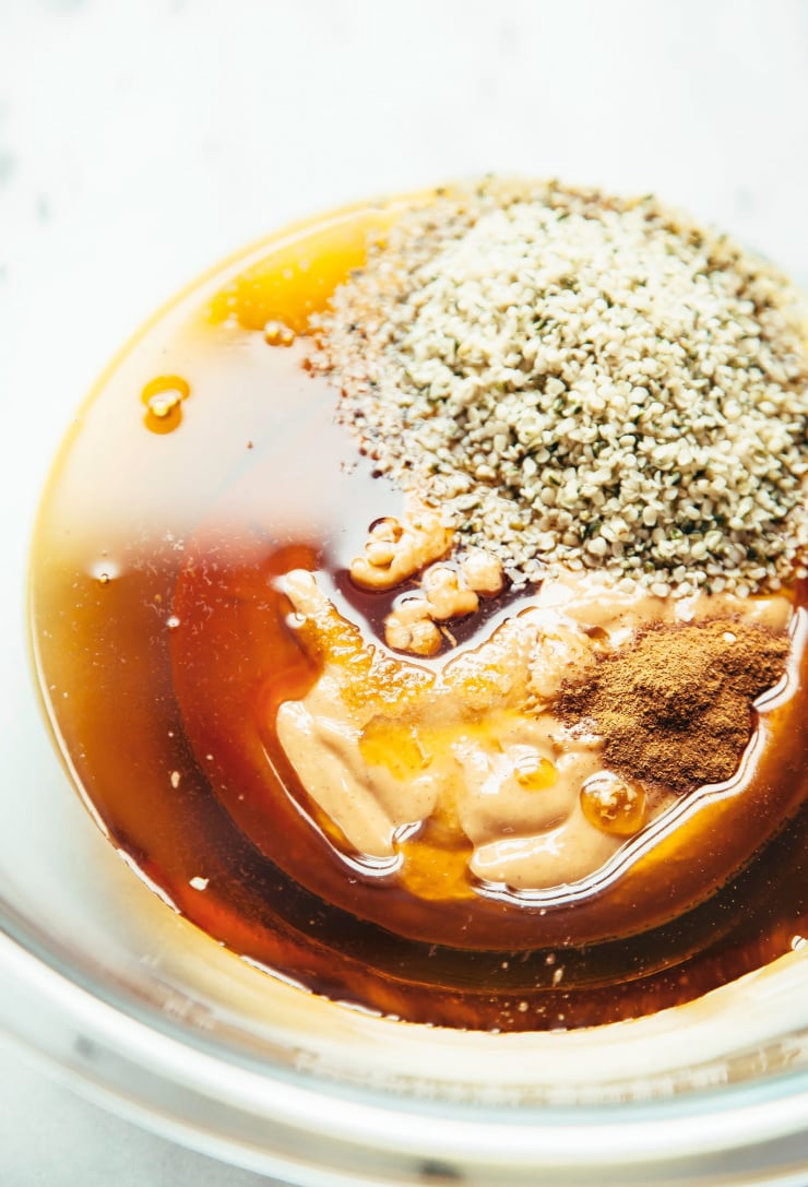 An up close, overhead image of maple syrup, nut butter, spices, and hemp seeds in a bowl.
