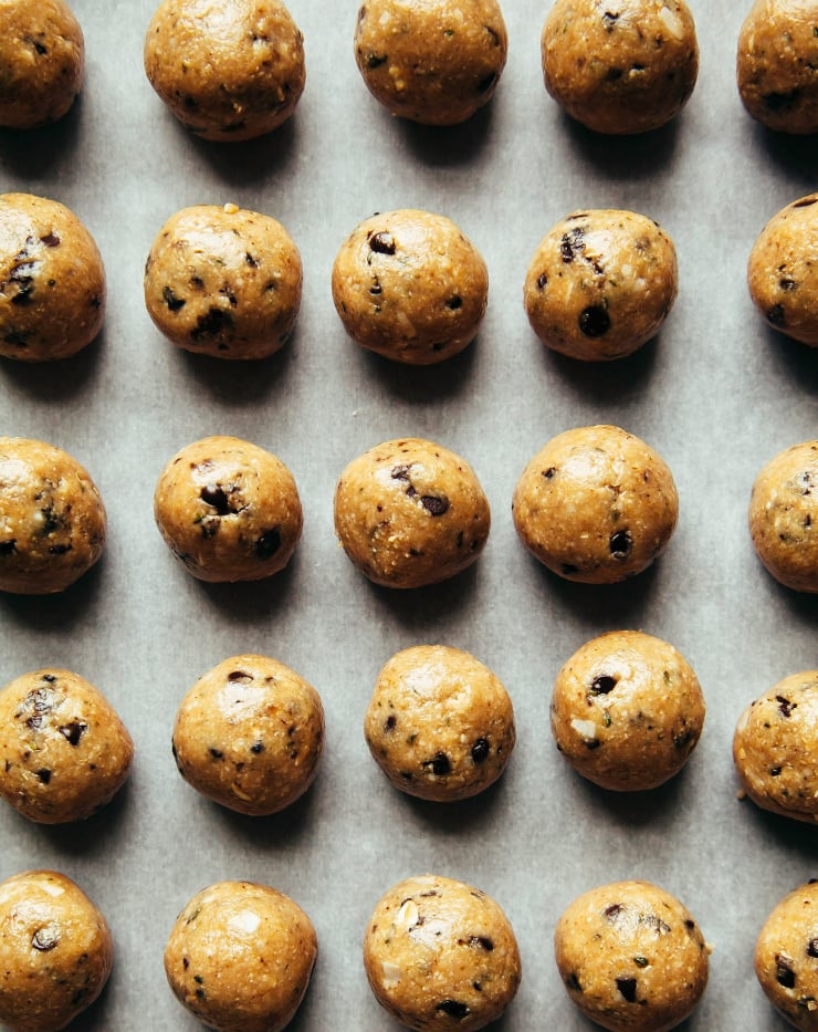 An overhead shot of rolled up cookie dough bites, all lined up on a sheet of parchment. There are flecks of chocolate chips in the golden, round bites.
