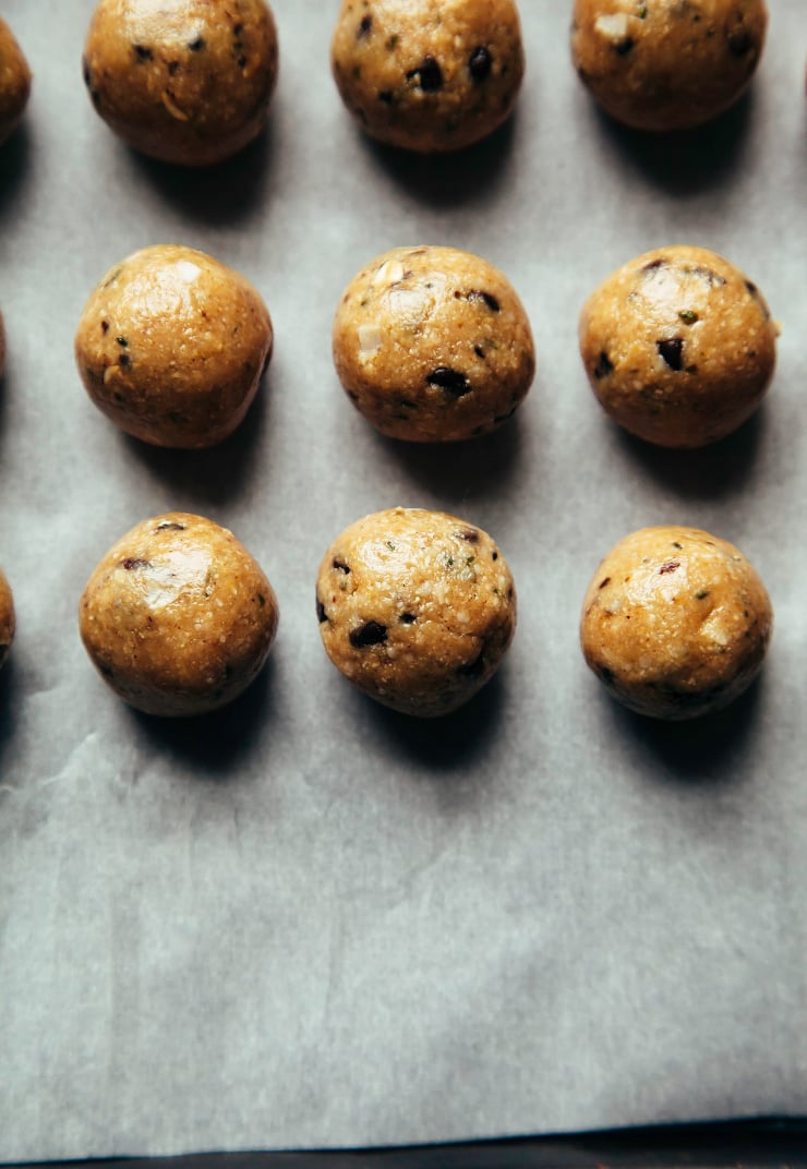 An overhead shot of rolled up cookie dough bites, all lined up on a sheet of parchment. There are flecks of chocolate chips in the golden, round bites.