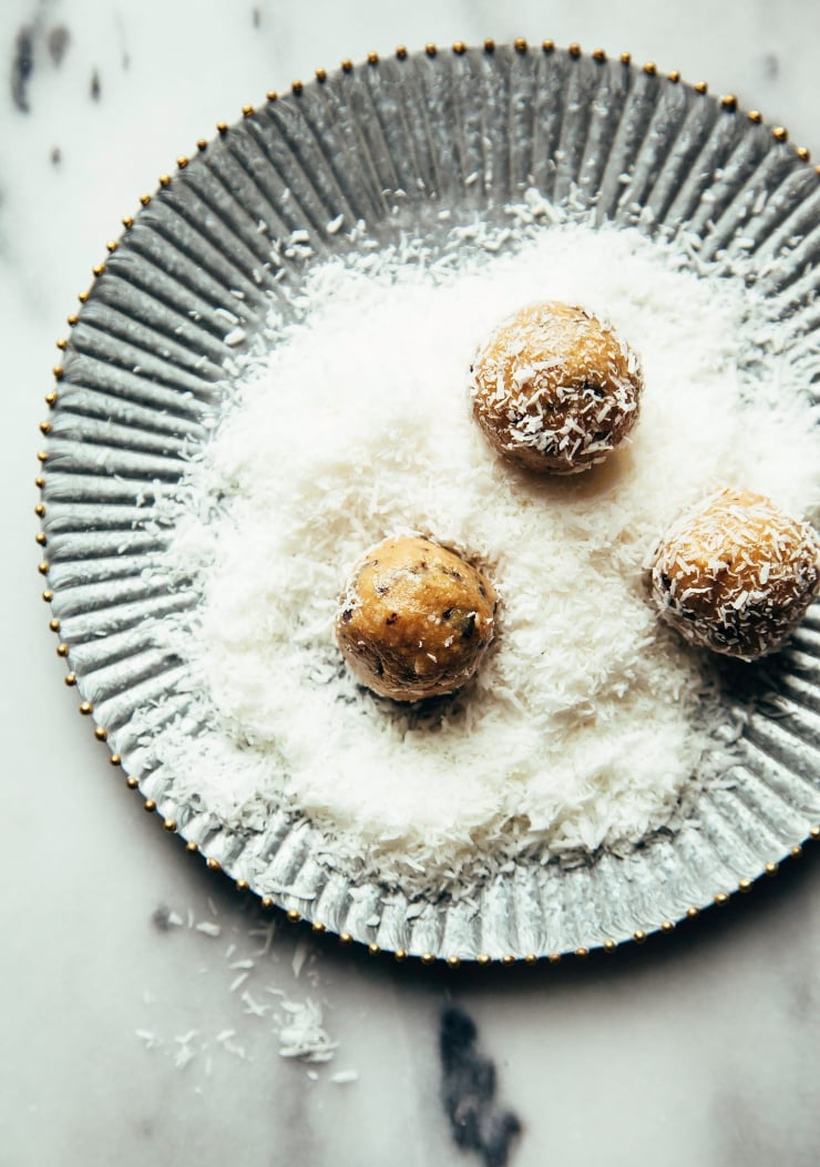 Overhead image shows balls of cookie dough rolling in shredded coconut on a metal plate.