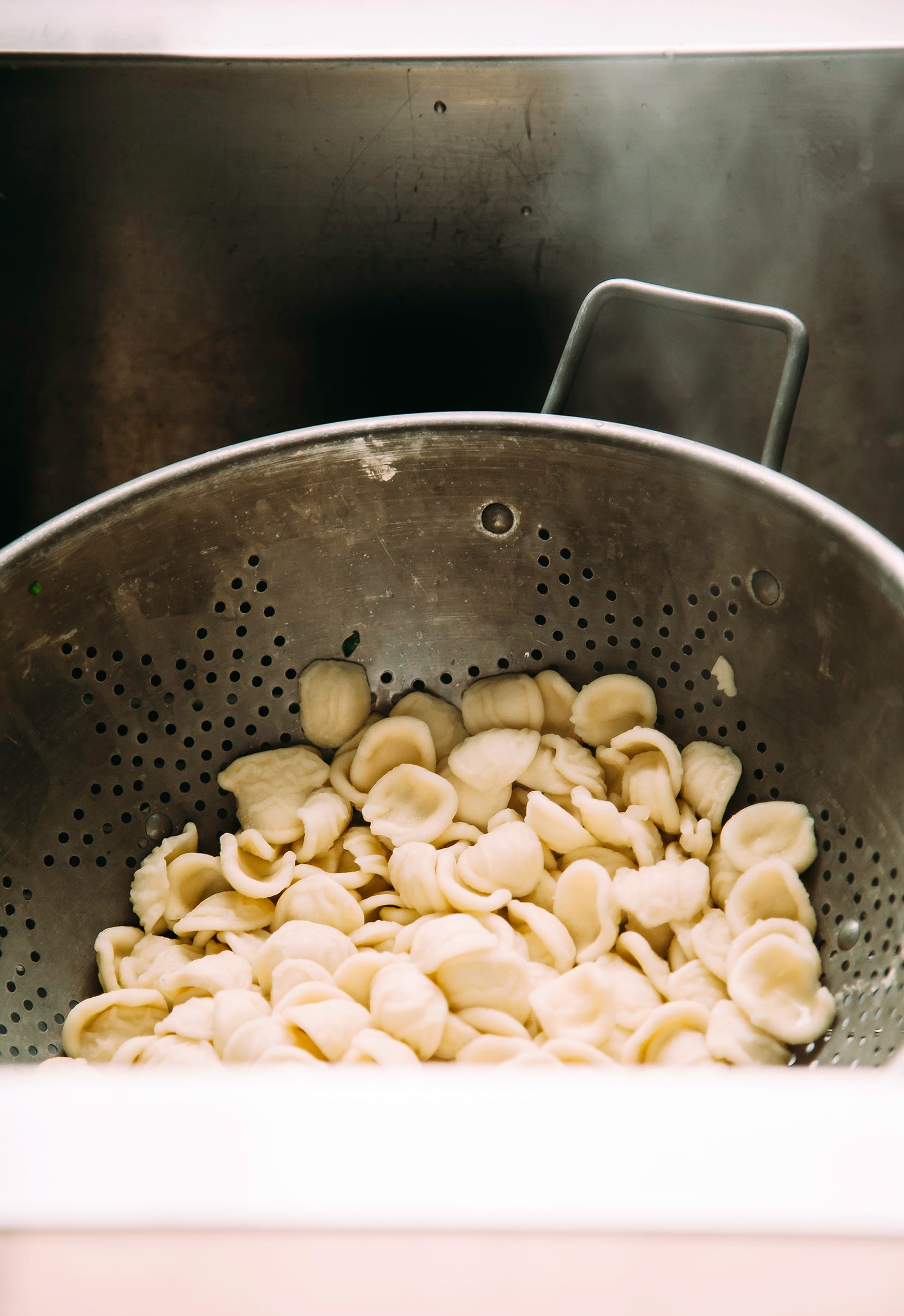 Image shows orecchiette pasta draining in a colander in a sink.