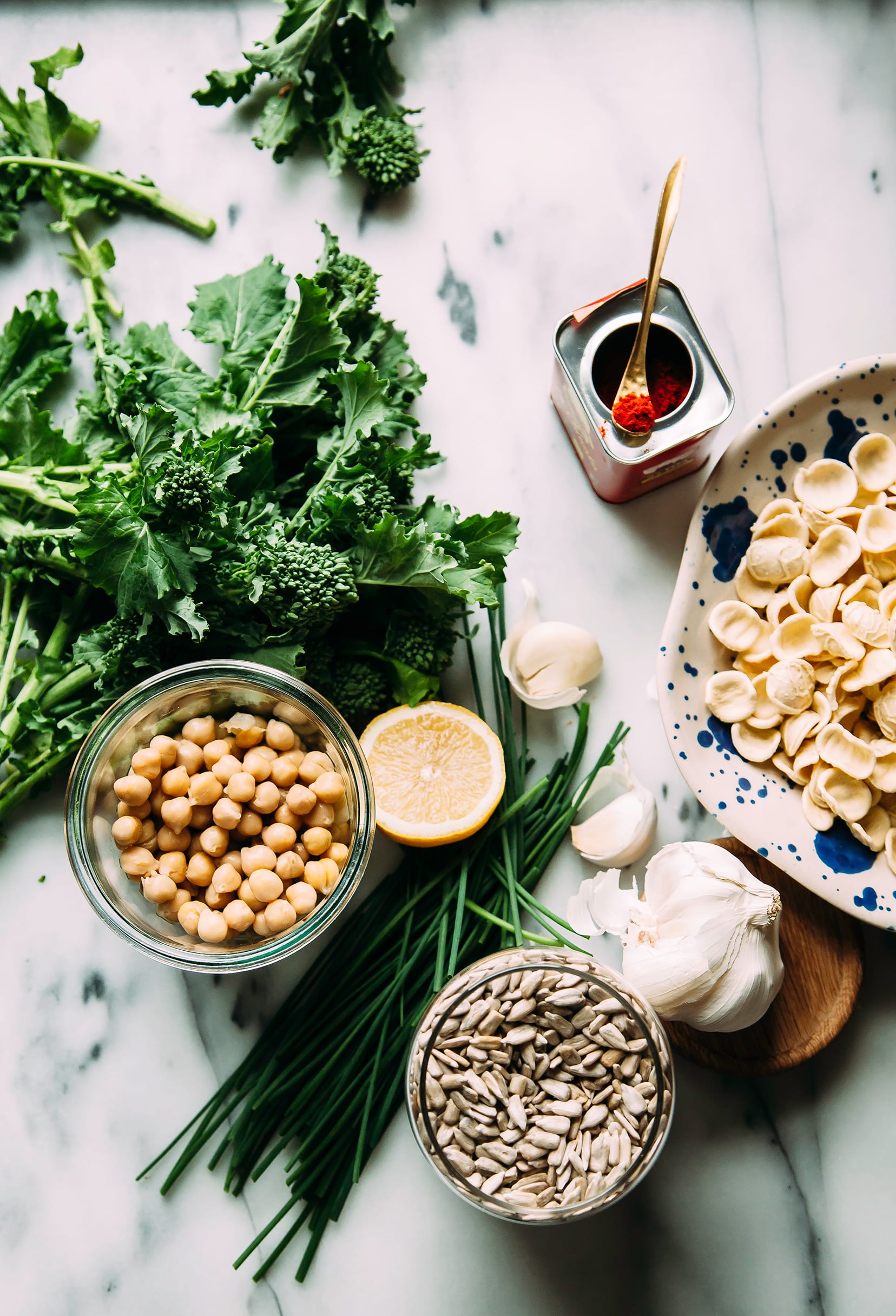 Overhead shot of ingredients for a broccoli rabe orecchiete pasta dish, all on a marble background.