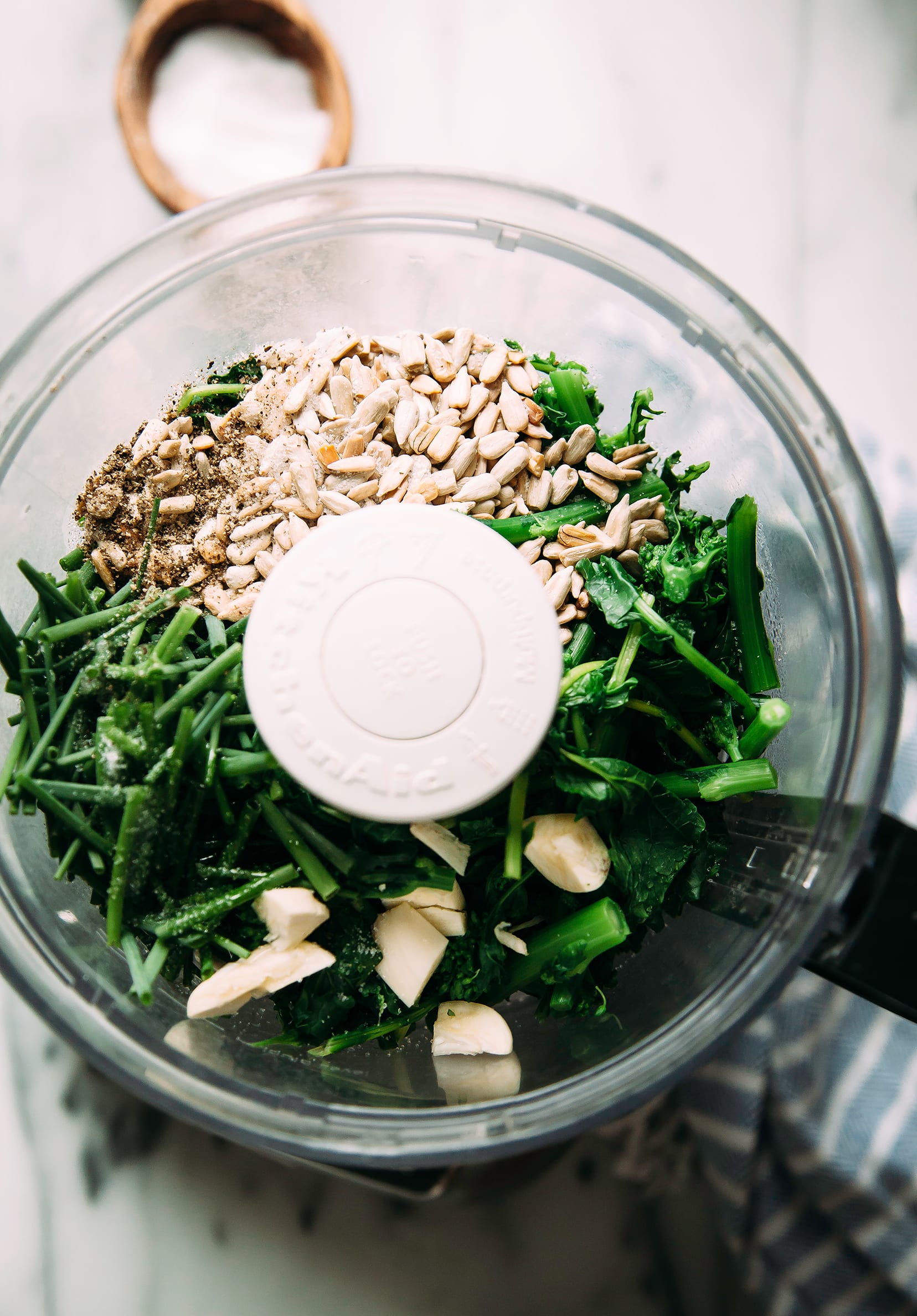 Image shows a food processor filled with ingredients for a broccoli rabe and chive pesto.
