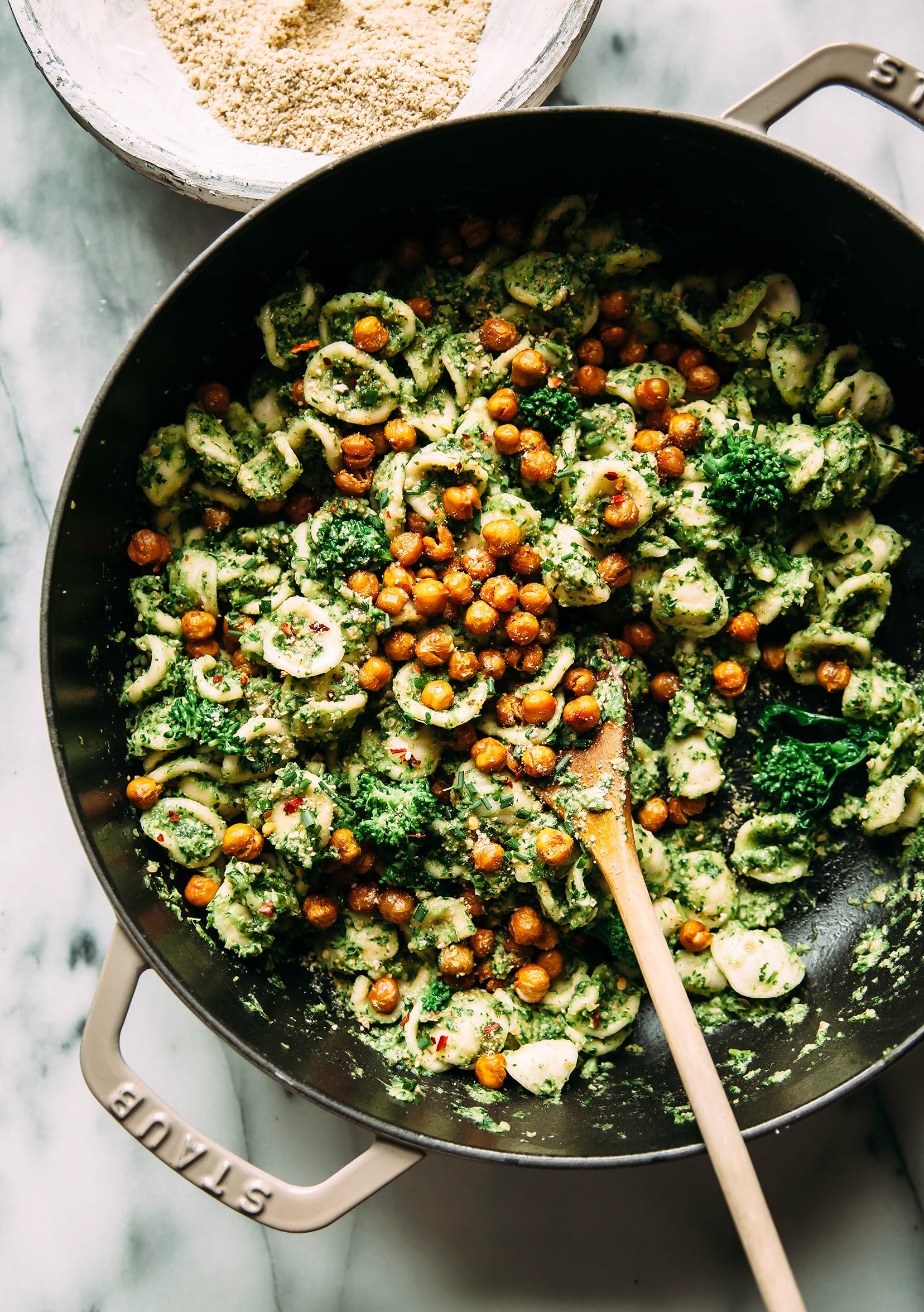 Image shows a shallow, braiser-style pot of orecchiette pasta with crispy chickpeas on top, in a green pesto sauce.
