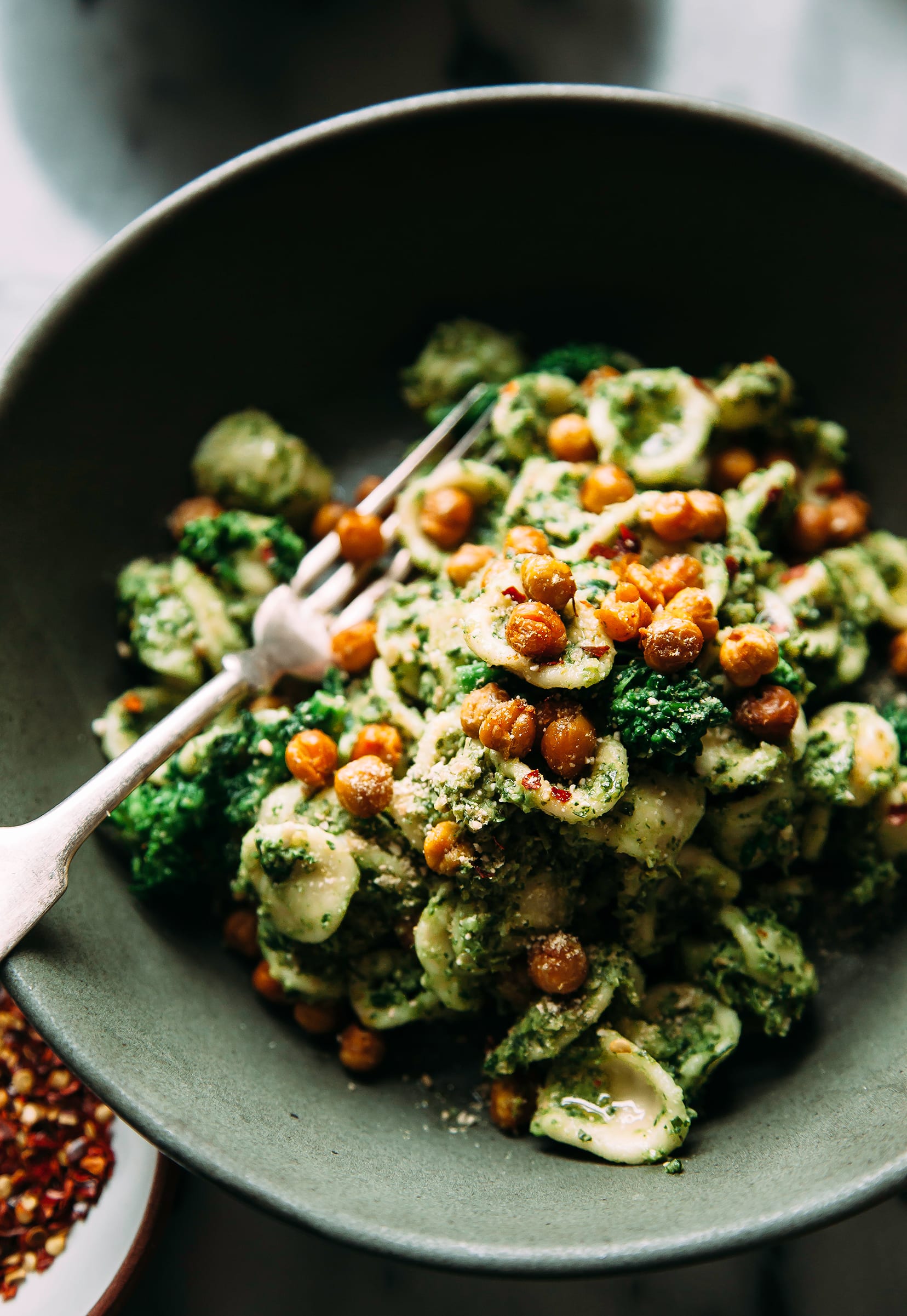 Image shows a bowl of orecchiette pasta with crispy chickpeas on top, in a green pesto sauce.