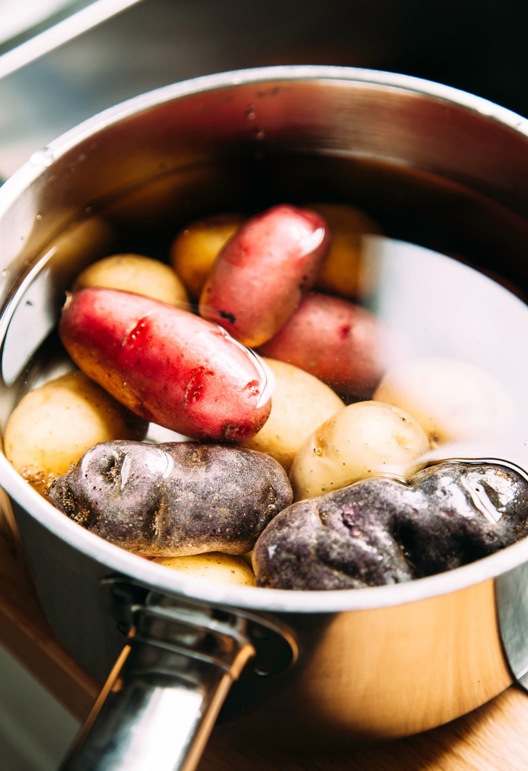 Image shows mini potatoes covered in water in a saucepan.