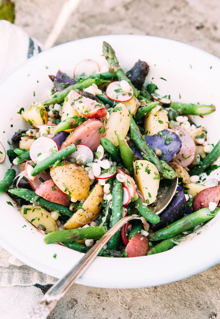 Image shows a bowl of a potato salad with asparagus, white beans and radishes.