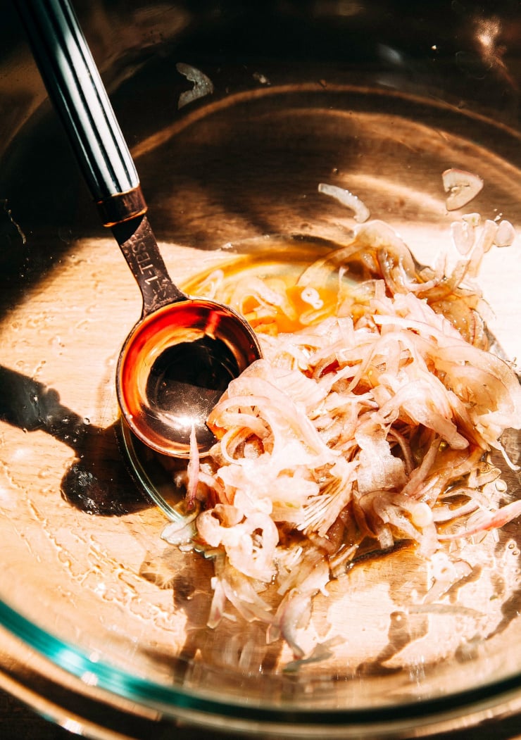Image shows thinly sliced shallots marinating in vinegar, in harsh sunlight.