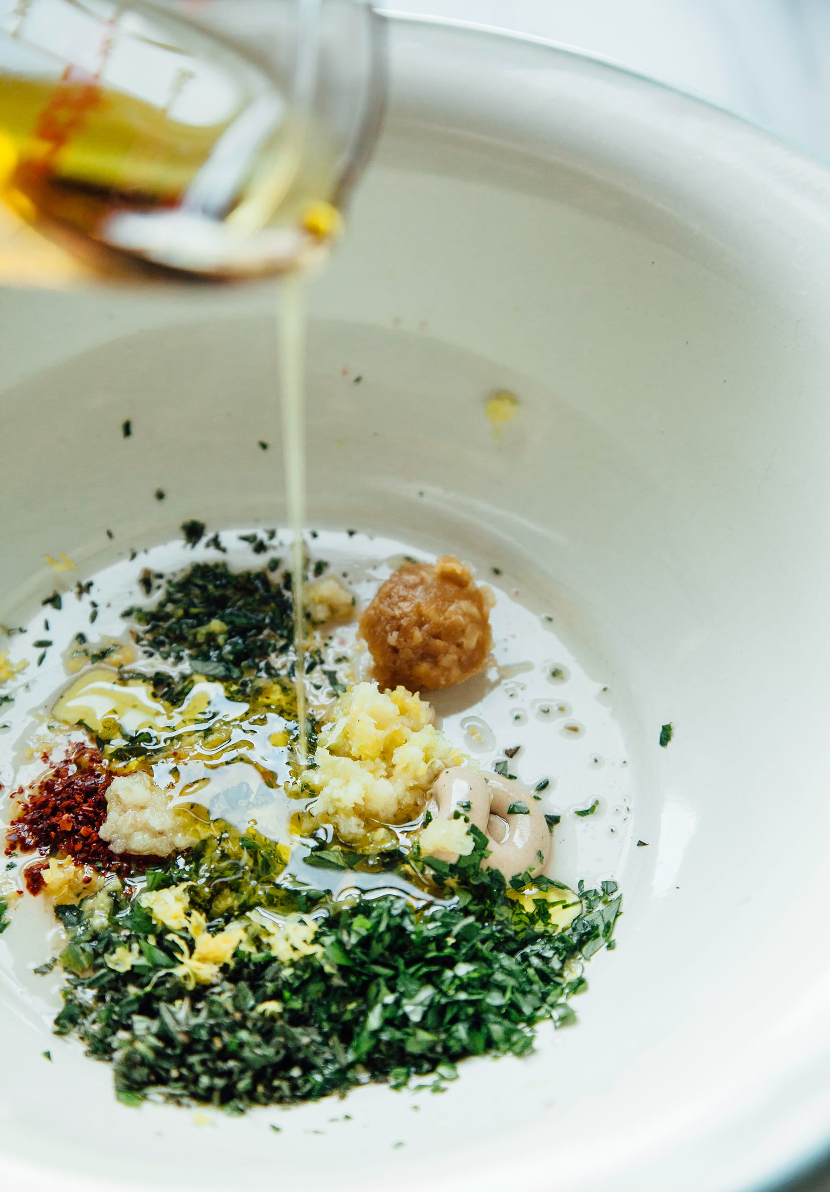 Image shows ingredients  for a marinade: chopped herbs, miso, garlic, chili flakes and olive oil.