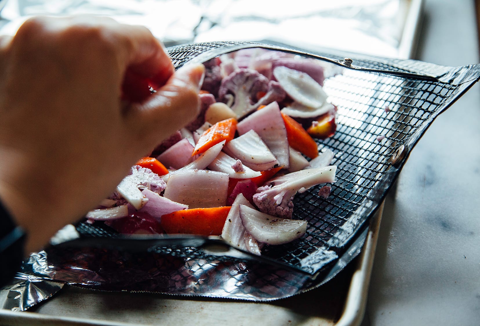 Image shows a hand holding a mesh grill bag open with vegetables inside.