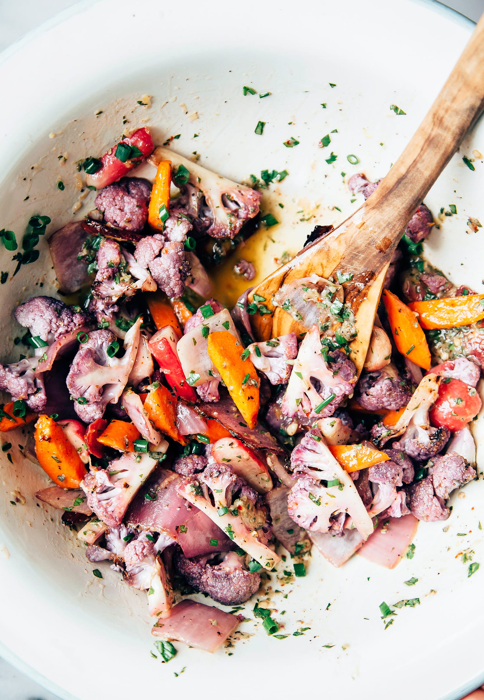 Image shows a bowl of mixed marinated vegetables: purple cauliflower, onions, carrots, and radishes; all flecked with herbs.