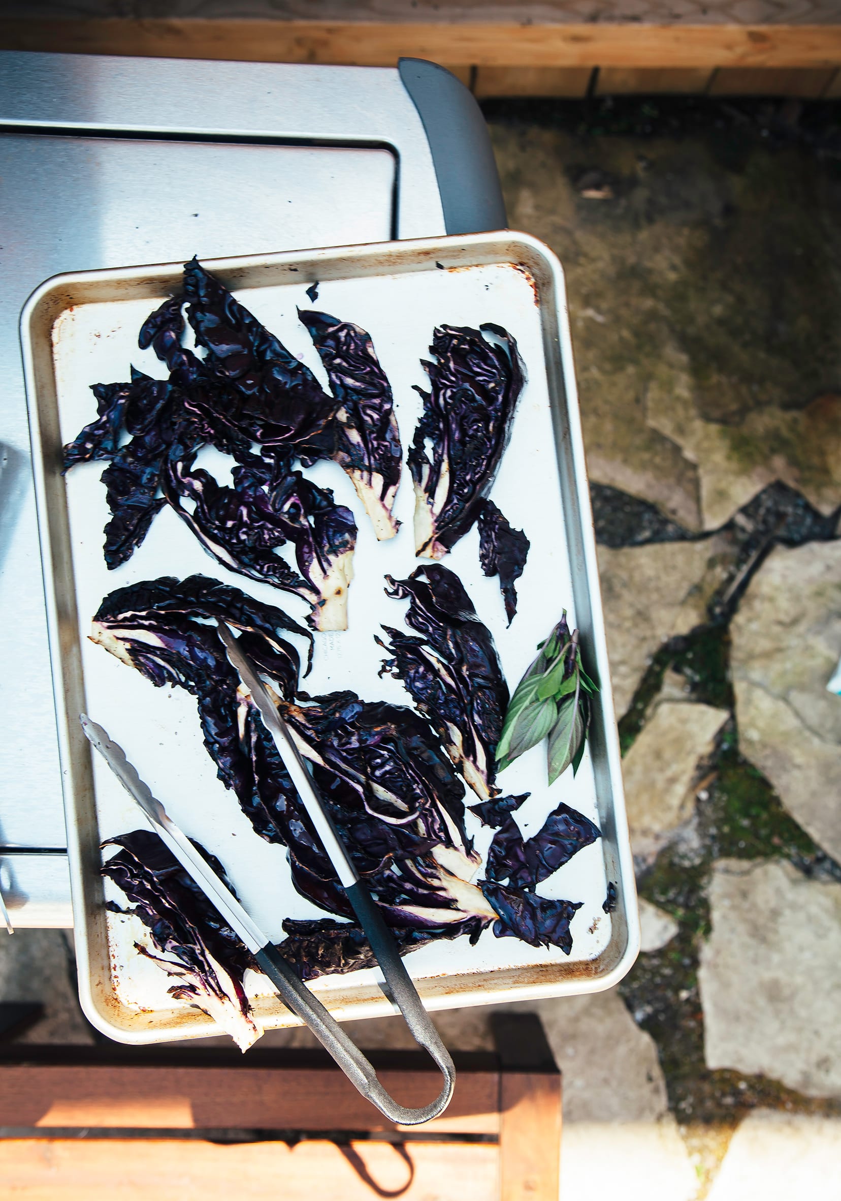 An overhead shot of grilled purple cabbage wedges on a baking sheet, outdoors.