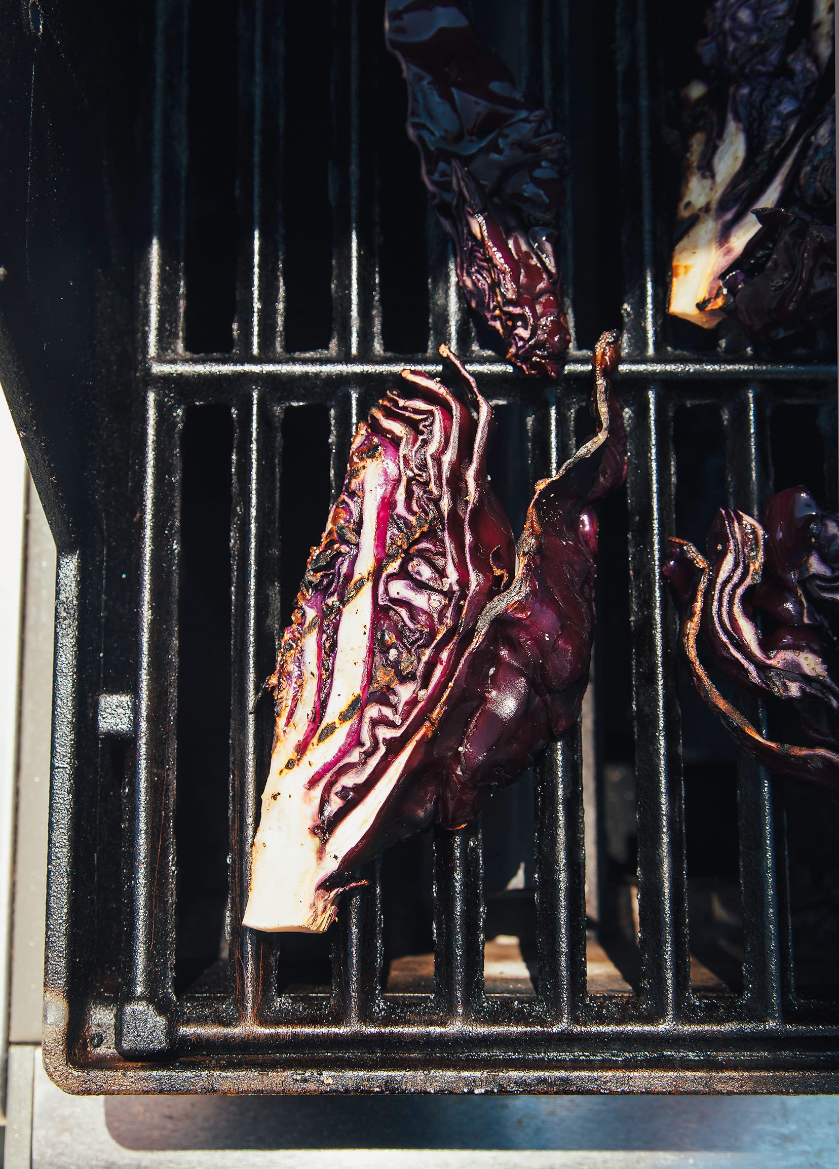Image shows wedges of purple cabbage grilling on a grill.